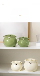 Ceramic seasoning jars in cream and green with lids and spoons on a shelf