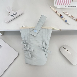 Flat lay of light blue quilted pencil case with bow details on a white desk with stationery