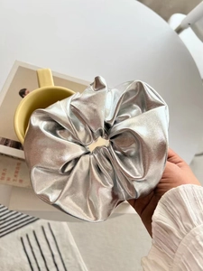 Close-up of a silver metallic fabric scrunchie with shiny pleated texture for hair