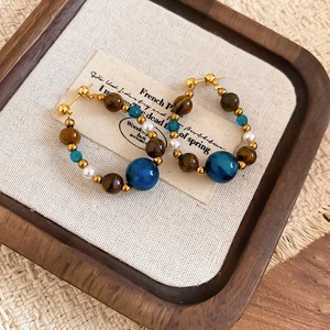 Detailed close-up of tiger eye and pearl hoop earrings on a beige textured jewelry tray