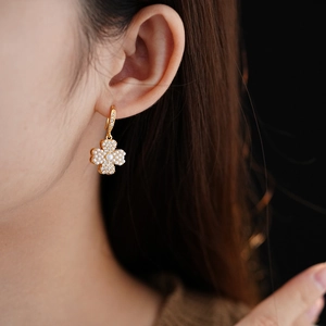 Detail shot of gold-plated clover earrings with white pearls and zircons on ear