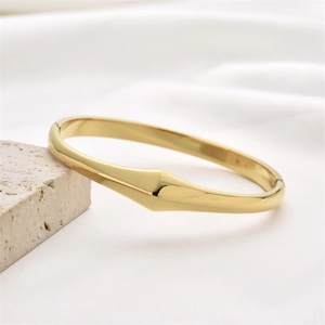 Minimalist hollow gold-plated stainless steel bangle on a modern white stone base