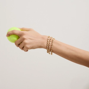 Detailed view of three stacked gold tennis bracelets with zircons on a model's wrist