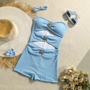 Flat lay of light blue seersucker swimsuit with golden sun buckles and vacation props