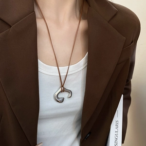 Close-up of irregular C-shaped silver pendant on a brown leather cord over a white ribbed top