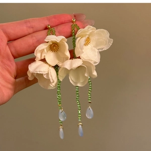 Primo piano degli orecchini a fiore in tessuto bianco con perline di vetro verdi.