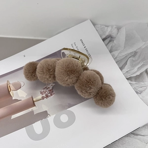 Detail of plush brown hair claw clip with seven pom-poms on a magazine background