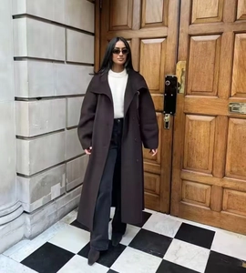Dettaglio di un lungo cappotto di lana marrone scuro con collo alto e cintura coordinata