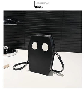 Detail view of a black coffin-shaped crossbody bag with white oval eye accents