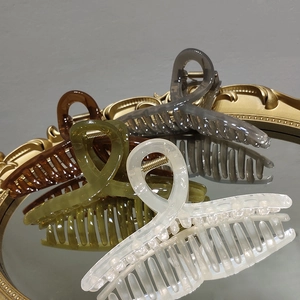 Detail view of large French jelly hair claws in amber and grey colors on a mirror