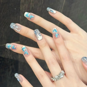 Detail of blue butterfly nail art with silver glitter and pearl accents on hands