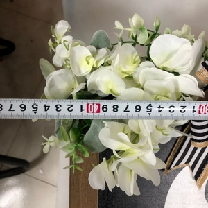Close-up of white artificial flower with green leaves being measured by a tape tool