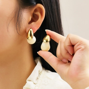 Gros plan de boucles d'oreilles dorées avec résine crème tenues entre les doigts