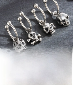 Detailed close-up of four silver titanium steel C-hoop earrings with skull charms for men