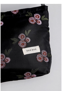 Close-up of black satin makeup bag with rose embroidery and H&R BAG woven label