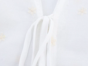 Détail du tissu en dentelle de coton blanc avec broderie florale et lien à nouer au cou