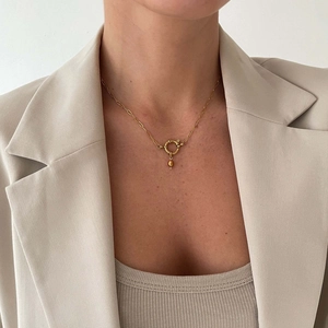 Close-up of a gold paperclip chain necklace with a bean pendant worn by a female model