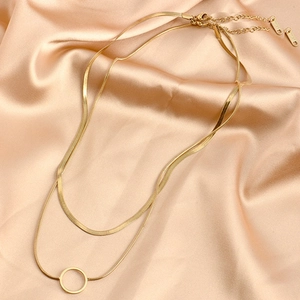 Double-layered gold snake chain necklace with circular pendant on golden silk fabric