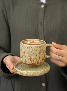 Close-up of hands holding a vintage stoneware coffee cup set with latte art detail