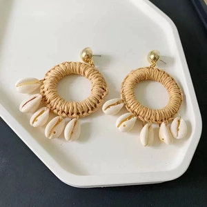 Detail of bohemian straw woven earrings with white shell pendants on a white tray