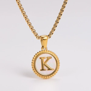 Macro detail of golden letter K pendant with pearl shell inlay and beaded circular edge
