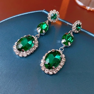 Vue macro de boucles d'oreilles ovales vert émeraude avec cristaux sur velours bleu