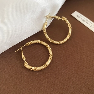 Macro detail of gold twisted rope hoop earrings with matte metallic texture and latch back