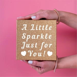 Close-up of hand holding a square golden glitter gift box with A Little Sparkle quote