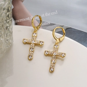 Boucles d'oreilles croix plaquées or avec zircons en forme de cœur sur fond blanc
