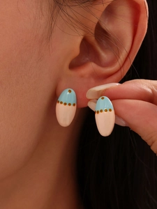 Close-up of pastel blue and pink enamel oval stud earrings on a model ear