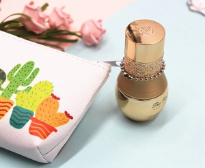 Detailed shot of cactus print makeup pouch and luxury gold skincare serum on pink background