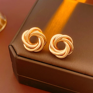 Close-up of gold geometric knot earrings placed on a premium dark brown leather jewelry box