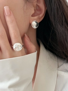 Close-up of elegant hammered silver geometric stud earrings and ring set on a model