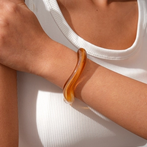 Close-up of amber acrylic irregular wavy bangle with glossy finish on a model's wrist
