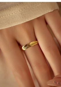 Macro close-up of a golden minimalist spiral texture ring worn on a hand with soft lighting