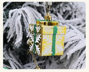 Close-up of golden Christmas gift box ornament with green glitter ribbon on snowy pine