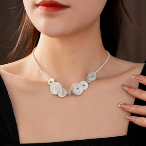Detail of beaded necklace featuring white shell pendants and colored beads on model