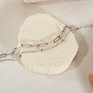 Close-up of double layer silver paperclip and bead chain on white stone display