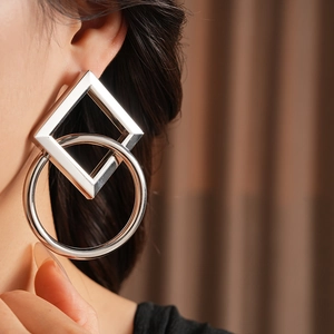 Gros plan de boucles d'oreilles géométriques argentées avec cadres carrés et ronds sur modèle