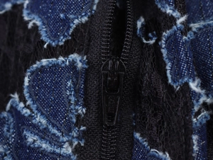 Macro shot of blue denim patchwork with black lace hollow embroidery and metal zipper
