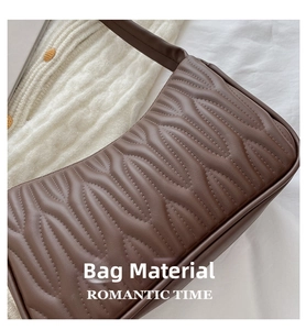 Close-up of brown wavy quilted leather shoulder bag on white knitted sweater fabric
