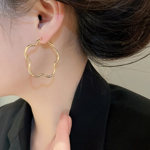 Close-up of a model wearing large hollow golden flower hoop earrings in a retro style