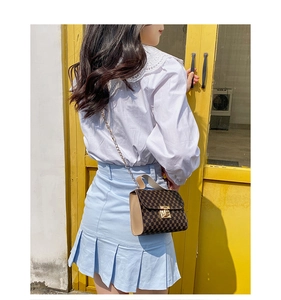 Brown monogram small square bag with golden lock shown on a model in outdoor setting