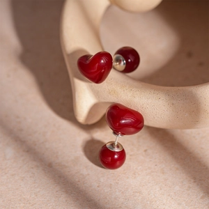 Détail de boucles d'oreilles cœur en résine rouge double face avec tiges en argent sur beige