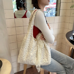 Close-up of a large floral canvas tote bag with lace charms worn by a model in a cafe
