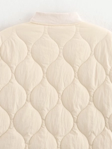 Close-up of cream quilted jacket featuring wave stitching and ribbed collar details