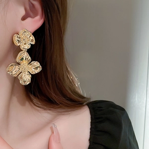 Close-up of golden metallic floral earrings worn by a model in a luxury side profile view