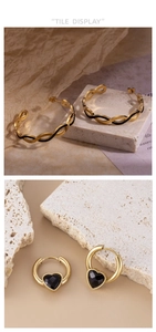 Detail of gold-plated wave hoop earrings and black heart pendant earring on stone