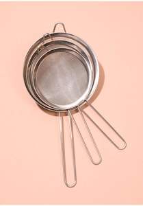 Three sizes of stainless steel mesh strainers with long handles on a pink background