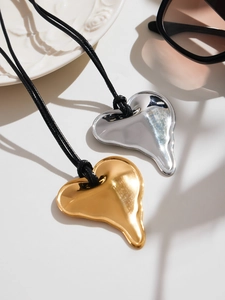 Detail of fluid heart-shaped pendants in gold and silver on black cord necklaces